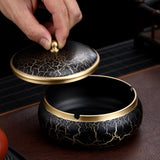 Black and gold ceramic ashtray with lid being held open by a hand