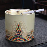 Decorative ashtray with intricate designs and a lit cigarette inside on a dark surface.