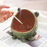 Frog-shaped ceramic ashtray with a hand placing a cigarette inside 