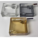 Three square glass ashtrays in different colors with cigarette rested on groove