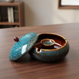 Large ceramic patio ashtray with lid open on wooden tabletop, blue speckled smokeless ashtray for outdoor use