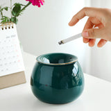 hand placing cigarette into green ashtray with funnel lid close up